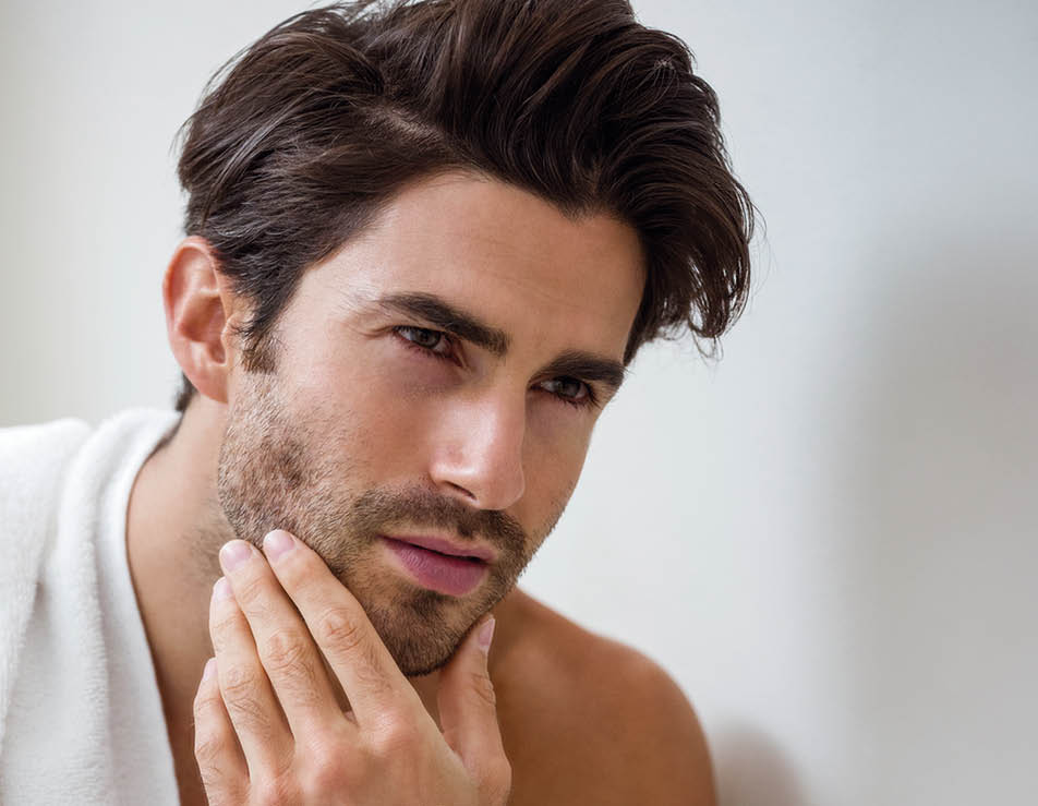 Close-up of young man looking checking his stubble in bathroom
