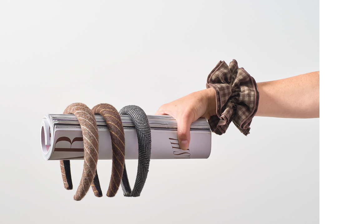 Una mano sostiene un rollo de papel envuelto con tres diademas de tela y una pulsera de tela a cuadros en la mu eca. Descripci n generada con IA
