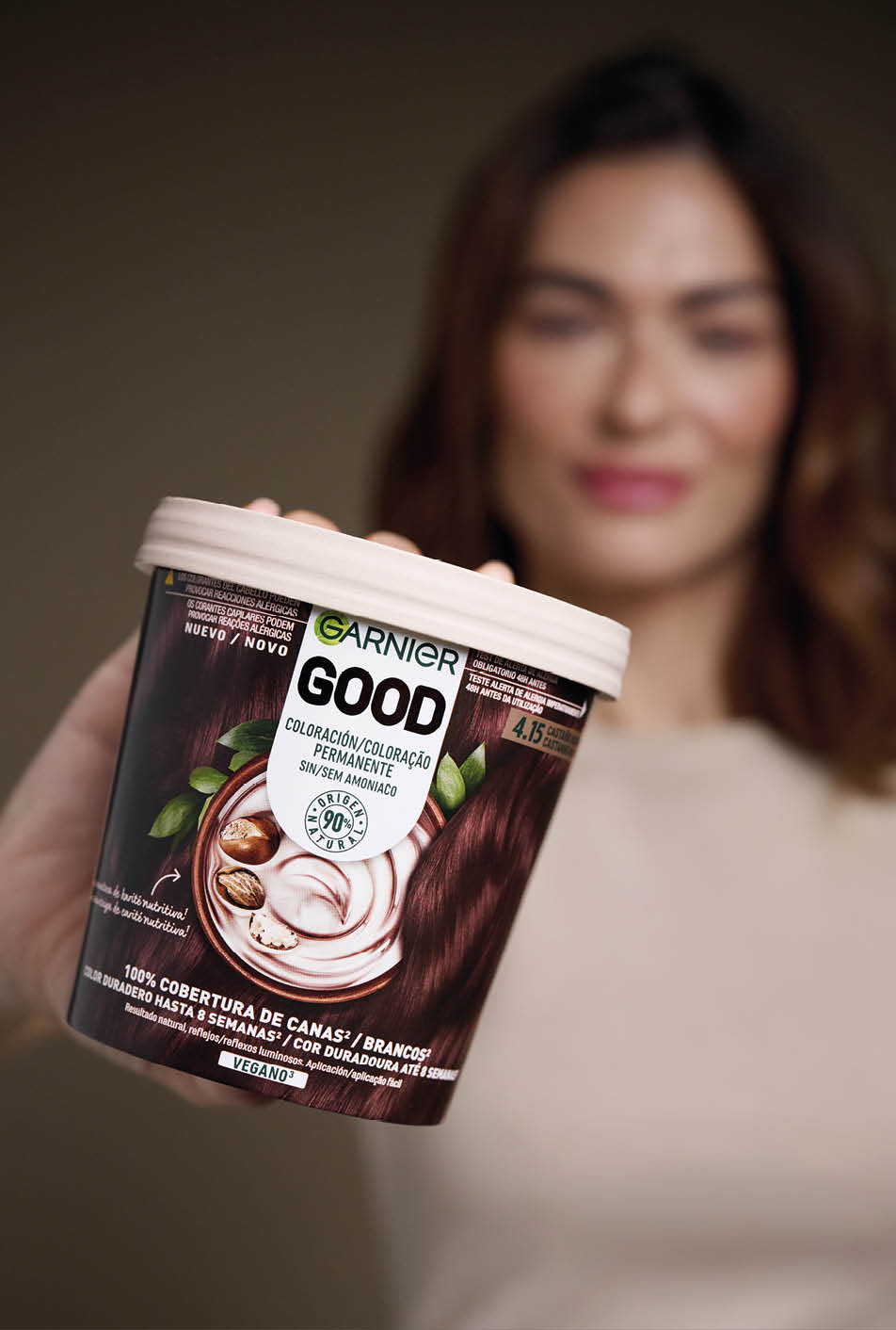 Persona sosteniendo un envase de coloraci n permanente para el cabello de la marca Garnier Good con imagen de cabello casta o y nueces en el empaque. Descripci n generada con IA