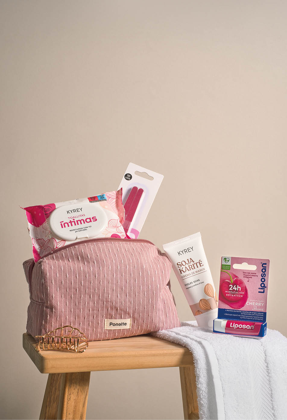 Neceser rosa con textura de rayas blancas sobre una mesa de madera que contiene toallitas h medas, crema corporal, b lsamo labial y una toalla blanca. Descripci n generada con IA