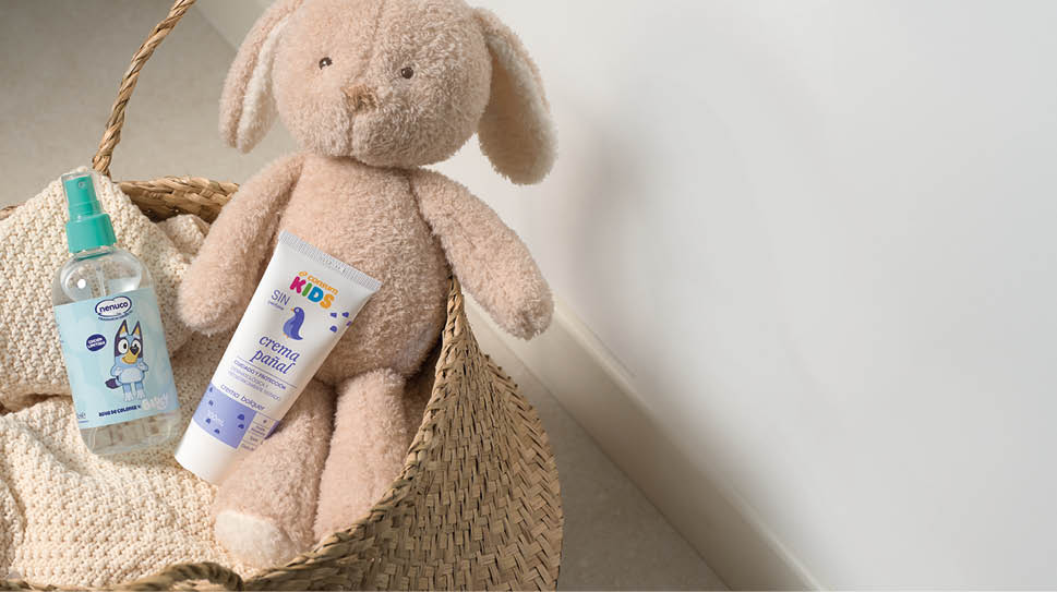 Un peluche en forma de perro est sentado dentro de una cesta de mimbre junto a dos productos infantiles para el cuidado de la piel.  Descripci n generada con IA