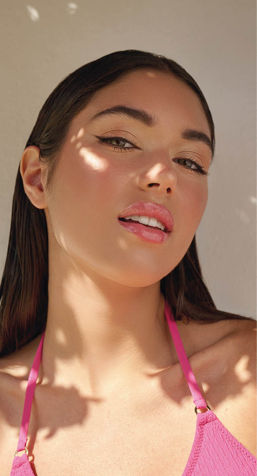 Persona con cabello largo y lacio usando un top rosa con tirantes finos, con luz y sombras proyectadas sobre la piel. Descripci n generada con IA