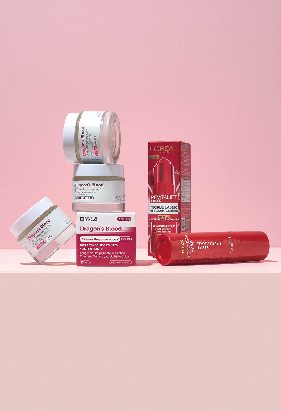 Varios productos cosm ticos de la l nea Dragon's Blood y Revitalift de L'Or al est n dispuestos sobre una superficie con fondo rosa. Descripci n generada con IA