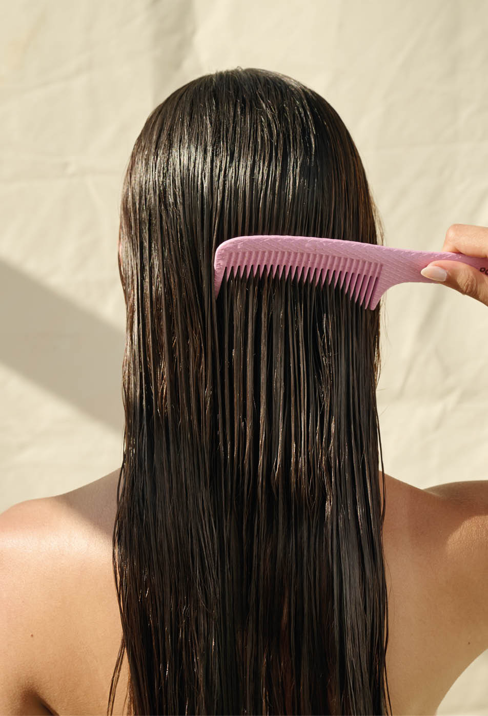 Persona con el cabello largo y mojado siendo peinado con un peine rosa de dientes anchos. Descripci n generada con IA