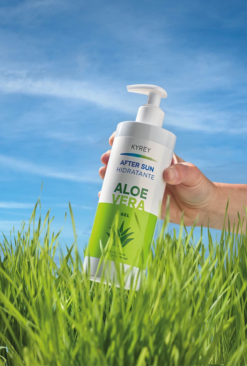 Una mano sostiene un envase con dispensador de gel hidratante de aloe vera para despu s del sol entre hierba verde bajo un cielo azul despejado. Descripci n generada con IA