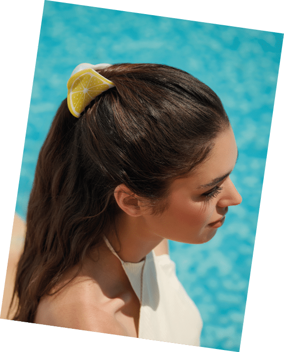 Persona con cabello largo recogido con un accesorio en forma de rodaja de lim n junto a una piscina con agua azul. Descripci n generada con IA