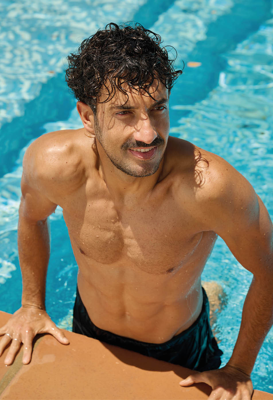 Una persona con cabello rizado y traje de ba o oscuro est saliendo de una piscina apoy ndose en el borde.  Descripci n generada con IA