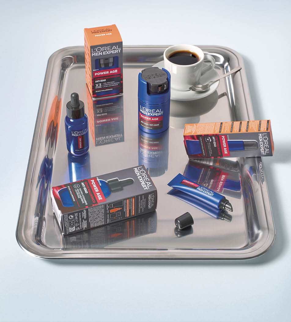 Varios productos de cuidado facial de la l nea L'Or al Men Expert Power Age est n dispuestos sobre una bandeja met lica junto a una taza de caf con platillo y cuchara.  Descripci n generada con IA